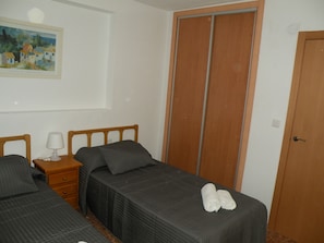 A bedroom with two beds, a nightstand, a lamp, a painting, and a wardrobe. - Gijon 9B in Benidorm (Benidorm)
