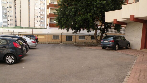 Ein Parkplatz mit mehreren Autos, einem Baum und einem Gebäude mit Ziegelverkleidung.