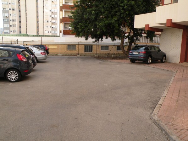 Zona aparcament amb diversos cotxes, un arbre i un edifici amb façana de maó.