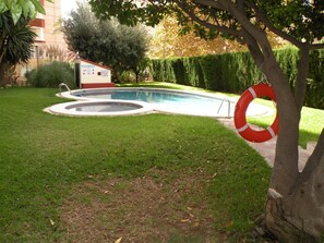Ein Schwimmbad mit Rettungsboje, umgeben von einer gepflegten Rasenfläche und einem Gebäude im Hintergrund.