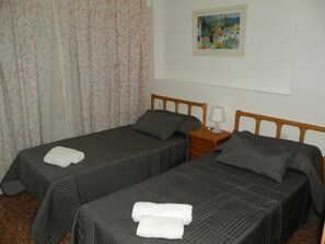 Ein Hotelzimmer mit zwei Einzelbetten, jeweils mit Kissen und Handtuch. Dazwischen steht ein Nachttisch mit einer Lampe. Über den Betten hängt ein Gemälde.