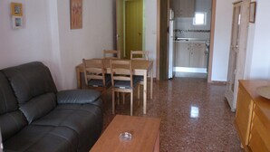 A living room with a black sofa, a wooden dining table with chairs, a kitchen in the background, and a door leading to another room. - Gijon 9B in Benidorm (Benidorm)