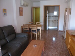 Ein Wohnzimmer mit einer schwarzen Couch, einem Holzespeisetisch mit Stühlen, einer Küche im Hintergrund und einer Tür zu einem anderen Raum.