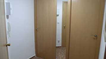 Um quarto com duas portas de madeira, uma parede branca e um chão de azulejos.