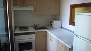A compact kitchen with wooden cabinets, a built-in microwave, a sink, and a stove. - Finlandia 10D in Benidorm (Benidorm)