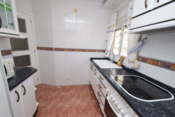 A kitchen with white cabinets, a black countertop, a stove, and a sink. - Adelfas 10D in Benidorm (Benidorm)