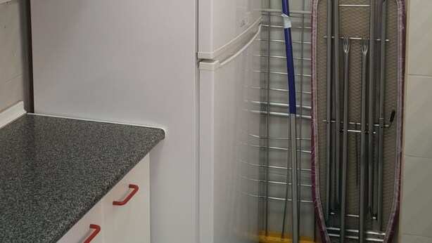 Eine kleine Küche mit weißen Schränken, einem Kühlschrank, einer Arbeitsplatte aus Granit und einem Wischmop-Ständer.