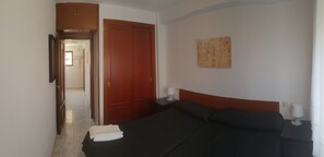 A hotel room with a bed, a wooden door, a painting on the wall, and a nightstand with a lamp. - Gemelos 12 2D1 in Benidorm (Benidorm)