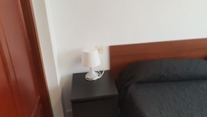 Ein Bett mit dunkler Bettdecke, eine weiße Nachttischlampe auf einem schwarzen Nachttisch und ein Holz-Kopfteil.