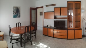 Ein Wohnzimmer mit Fernseher, einem Esstisch mit Stühlen, einer Couch und einer Lampe.