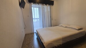A bedroom with a bed, a window with curtains, a wall-mounted TV, and a power outlet. - Mariscal 3 4J 2 Dormitorios (Benidorm)