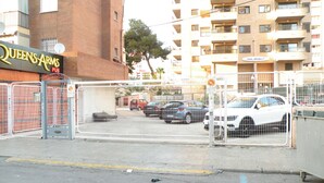 A gated parking area with multiple cars, a building with a sign reading "Queens Arms Pub," and a multi-story residential building in the background. - Karola 8D in Benidorm (Benidorm)
