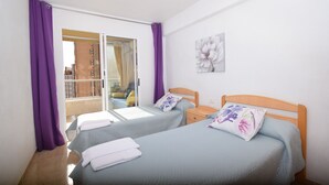 A bedroom with two beds, purple curtains, a wooden headboard, a window, and a wall-mounted artwork. - Karola 8D in Benidorm (Benidorm)