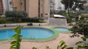 A pool area with two pools, surrounded by greenery and a building in the background. - Karola 8D in Benidorm (Benidorm)