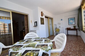 A dining area with a table covered in a tablecloth with olive images, white chairs, and a window with curtains. - Mariscal 1 10C in Benidorm (Benidorm)