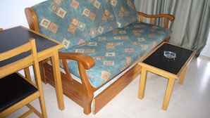Un sofá de madera con un cojín estampado, dos mesitas de noche de madera y un cenicero de vidrio.