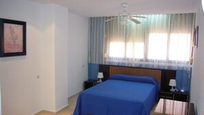 Un dormitorio con una cama, dos mesitas de noche, un ventilador de techo y una ventana con cortinas.