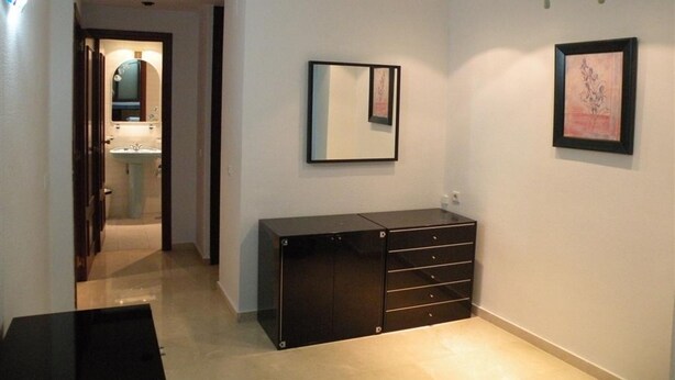 Un pasillo con un mueble negro, un espejo y un cuadro en la pared.