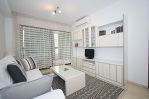 A modern living room with a white sofa, a glass coffee table, a flat-screen TV, and a built-in bookshelf.