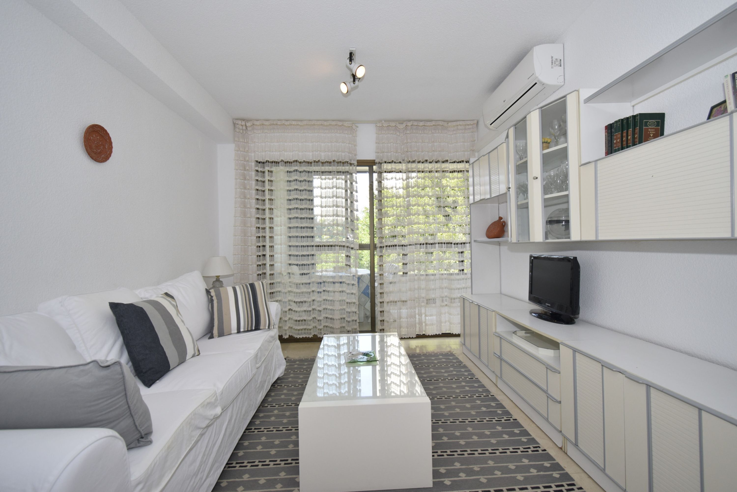 A modern living room with a white sofa, a coffee table, and a television on a cabinet.