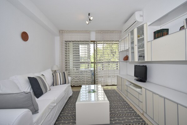 A modern living room with a white sofa, a coffee table, and a television on a cabinet.