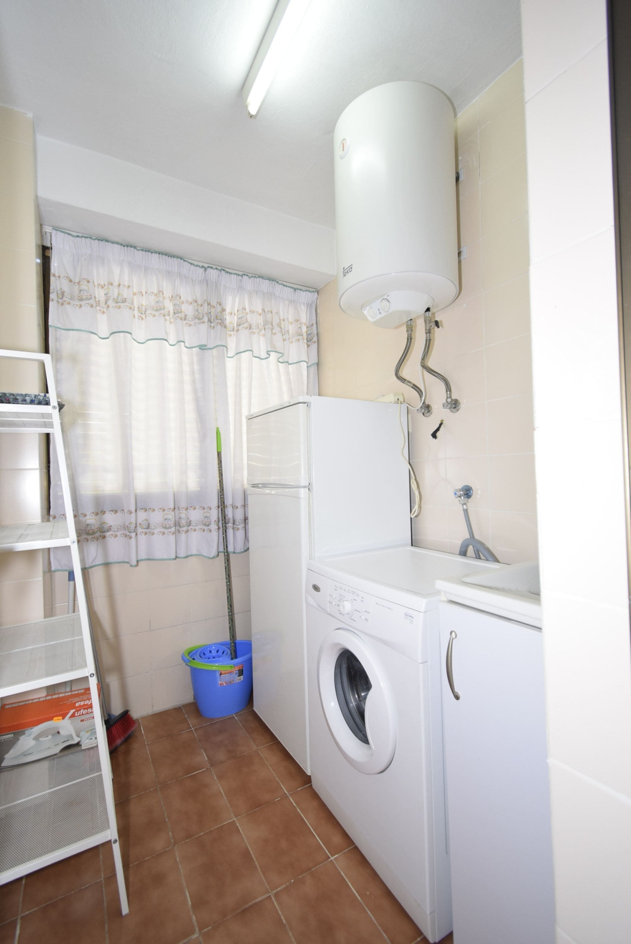 A compact laundry room with a washing machine, a drying rack, and a ceiling-mounted water heater.