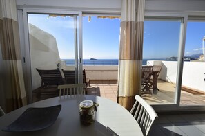 A balcony with a table, chairs, and a view of the sea.