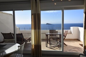 A balcony with a table and chairs, a view of the sea, and a distant island.