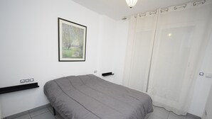 A bedroom with a bed, a framed picture on the wall, a shelf, and a door with a curtain. - Villamarina A517 in Benidorm (Benidorm)