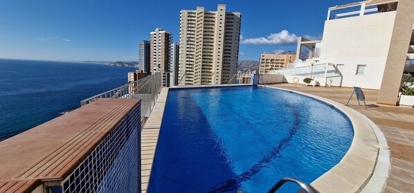 A rooftop swimming pool with a view of the ocean and high-rise buildings.