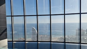 Vista a través de un ventanal con diseño de cuadrícula, con vistas a una zona costera con edificios y cielo despejado.