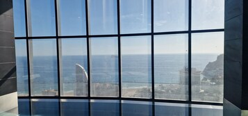 A view through a large window with a grid pattern, overlooking a coastal area with buildings and a clear sky.