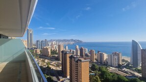 Un edificio alto con vistas a una ciudad costera, incluyendo una playa y una cadena montañosa en la distancia.