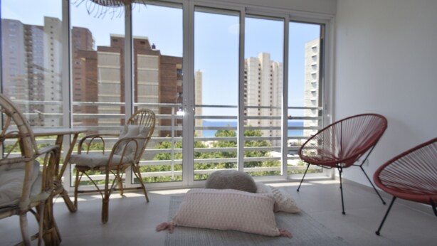 Een balkon met rieten stoelen, een tafel en uitzicht op gebouwen en water.