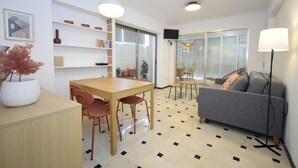 Een moderne woonkamer met een bank, een eettafel met stoelen, een salontafel, een lamp en een boekenkast.