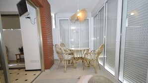 Een eetgedeelte met een ronde tafel en vier rieten stoelen, een geweven lamp en een schuifdeur met geëtste glaspanelen.