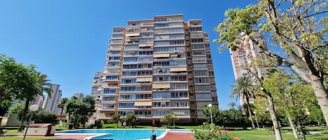 A high-rise apartment building with multiple balconies, a swimming pool, and surrounding greenery.