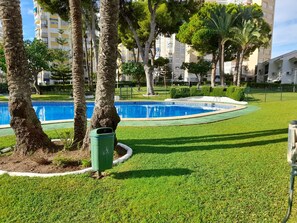 A swimming pool surrounded by well-maintained grass and trees, with a building in the background. - Urbanizacion Miramar 1057 (Benidorm)