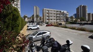 A parking lot with several cars and motorcycles, a multi-story building in the background, and some greenery on the left. - Mariscal 4 4C in Benidorm (Benidorm)