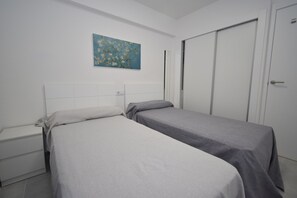 A room with two single beds, a nightstand, a wardrobe, and a painting on the wall. - Mariscal 4 4C in Benidorm (Benidorm)