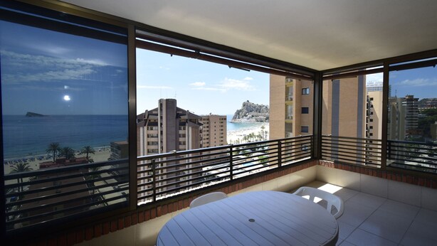 A balcony with a table and chairs, overlooking a beach and buildings. - Castelmar 8B in Benidorm (Benidorm)