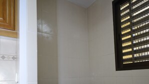 A compact laundry room with a front-loading washing machine, tiled walls, a wooden cabinet, and a window with blinds. - Castelmar 8B in Benidorm (Benidorm)