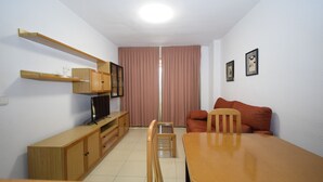A compact living space with a wooden dining table, a television on a wooden stand, a red sofa, and a small wooden cabinet. - Castelmar 8B in Benidorm (Benidorm)
