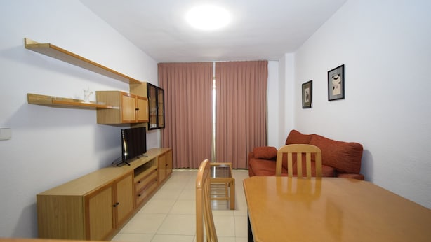 A compact living space with a wooden dining table, a television on a wooden stand, a red sofa, and a small wooden cabinet. - Castelmar 8B in Benidorm (Benidorm)