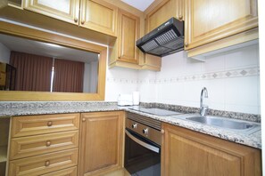 A kitchen with wooden cabinets, a granite countertop, a stainless steel sink, and a built-in oven. - Castelmar 8B in Benidorm (Benidorm)