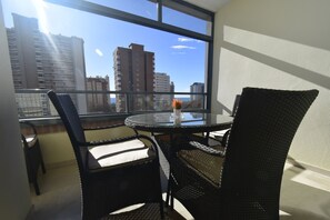 Ein Balkon mit Tisch und Stühlen, eine Vase mit Blumen und Blick auf die Stadt durch große Fenster.