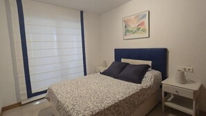 A bedroom with a bed, a nightstand, a wall-mounted painting, and a window with blinds. - Castelmar 1C in Benidorm (Benidorm)