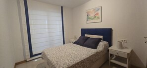 A bedroom with a bed, a nightstand, a wall-mounted painting, and a window with blinds. - Castelmar 1C in Benidorm (Benidorm)