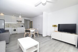 Uma sala de estar moderna com televisão de tela plana, área de jantar com mesa e cadeiras, sofá e cozinha com máquina de lavar.