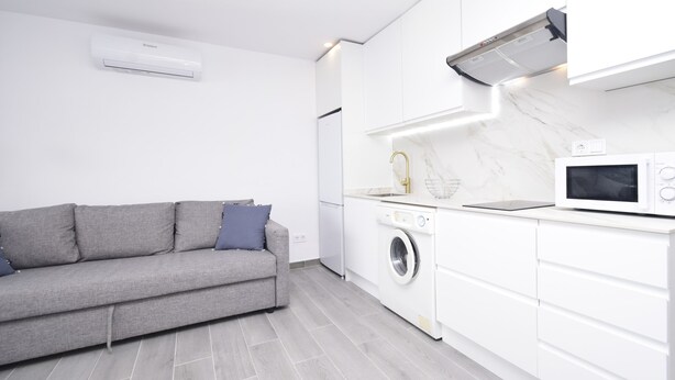 Une cuisine moderne avec des meubles blancs, un lave-linge encastré et un canapé gris agrémenté de coussins.